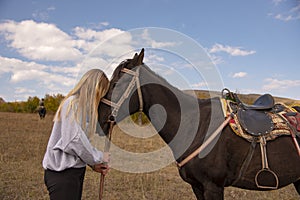 A teenage blonde girl holds the horse`s bridle