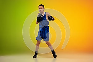 Teenage boxer against gradient neon studio background in motion of kicking, boxing