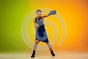 Teenage boxer against gradient neon studio background in motion of kicking, boxing