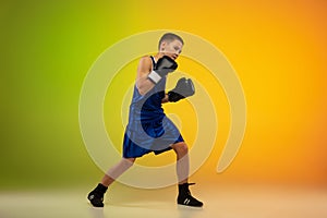 Teenage boxer against gradient neon studio background in motion of kicking, boxing