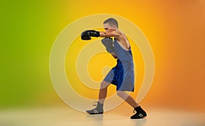 Teenage boxer against gradient neon studio background in motion of kicking, boxing