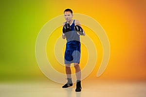 Teenage boxer against gradient neon studio background in motion of kicking, boxing