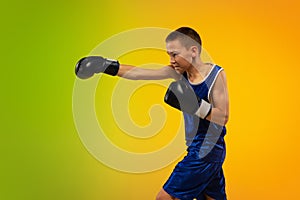 Teenage boxer against gradient neon studio background in motion of kicking, boxing