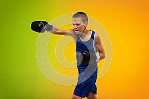 Teenage boxer against gradient neon studio background in motion of kicking, boxing