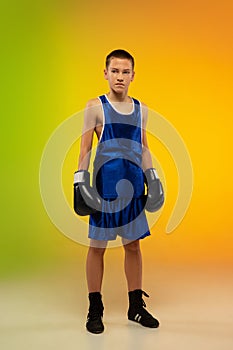 Teenage boxer against gradient neon studio background in motion of kicking, boxing