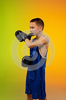 Teenage boxer against gradient neon studio background in motion of kicking, boxing