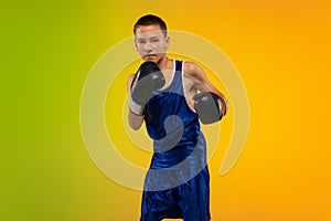 Teenage boxer against gradient neon studio background in motion of kicking, boxing