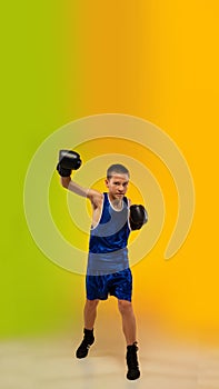 Teenage boxer against gradient neon studio background in motion of kicking, boxing