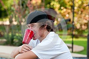 Teenage boy with acne and red cup in mouth looking at camera.