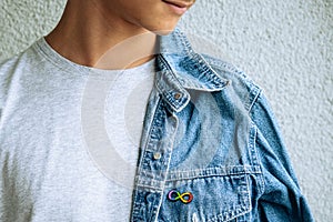 Teenage boy with autism infinity rainbow symbol sign metallic pin brooch on denim jacket. World autism awareness day