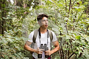 Teenage boy with binoculars hiking in forest. Summer vacation.