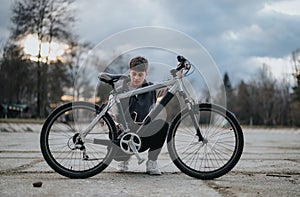 Teenage boy with a bicycle in a park during early evening