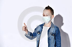 Teenage boy in a blue denim jacket, t-shirt. He is in a medical mask, showing thumb up