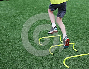 Teenage boy with both feet in the air jumping over mini yellow hurdles