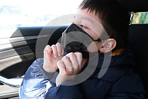 A teenage boy in car putting on surgical medical black face mask as a protection against virus disease, coronavirus covid 19