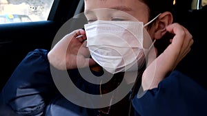 A teenage boy in car putting on white protective surgical medical face mask as a protection against virus disease, coronavirus pre