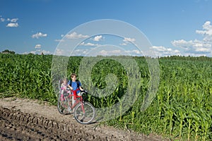 Teenage boy carrying his little sibling sister on baby bike seat on farm corn field summer dirt road photo