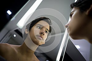 Teenage boy checking his skin in the mirror