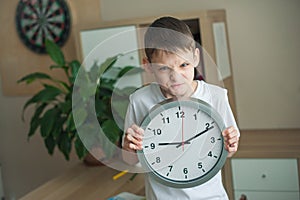 A teenage boy in a children`s room is standing with a big clock in his hands, he is very angry. The concept does not have time,