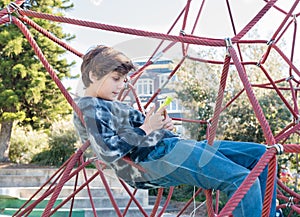 Teenage boy in climbing frame using smart phone