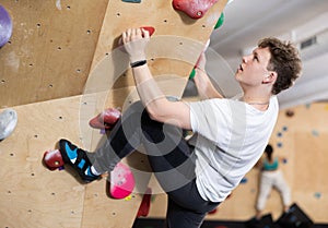 Teenage boy climbs steep artificial wall in sports complex and trains endurance