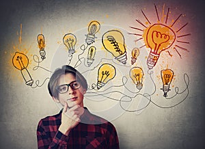 Teenage boy confident thinking, glowing light bulbs over head. Student guy dreamer wearing glasses, has different thoughts. Genius