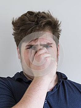 Teenage boy in dark blue shirt holding his nose to demonstrate bad smell