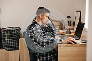 Teenage boy doing homework using computer sitting by desk in room alone