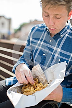 Teenage Boy Eating French Fries Sitting On Bench Outdoors
