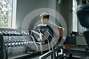 Teenage boy engaged in sports training with dumbbells at gym hall