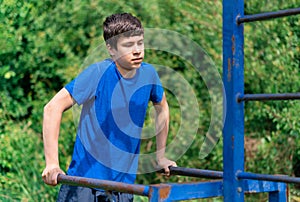 Teenage boy exercising outdoors, sports ground in the yard, he does push-ups at the bars, healthy lifestyle