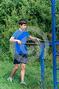 Teenage boy exercising outdoors, sports ground in the yard, he does push-ups at the bars, healthy lifestyle