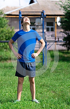 Teenage boy exercising outdoors, sports ground in the yard, he does a warm-up, healthy lifestyle
