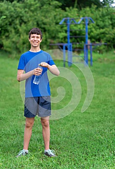 Teenage boy exercising outdoors, sports ground in the yard, he opens a bottle of water and drinks, healthy lifestyle