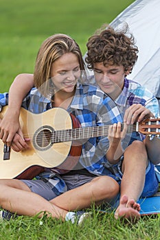 Teenage boy and girl near the tent playing a guitar outdoors