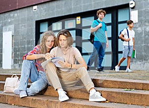 Teenage boy and girl sitting on steps near school