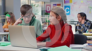 Teenage boy and girl study on laptop together sitting at desk in classroom