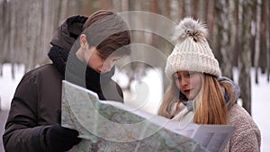 Teenage boy and girl talking examining paper map standing in winter park. Portrait of concentrated Caucasian teen couple