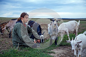 A teenage boy grazes goats in a field. A shepherd with goats in a field against a stormy sky.