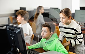 Teenage boy helping young girl with PC problem in computer class