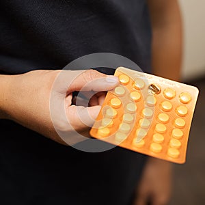 A teenage boy holds an orange pack of pill blisters in his hand. Panacea, medication, vitamins, healing from diseases, the concept
