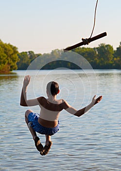 Teenage boy jumping in the river from the rope
