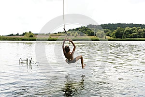 Teenage boy jumping in the river from the swinging rope on sunny summer day