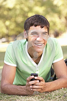 Teenage Boy Laying In Park Reading Text Message On Mobile Phone