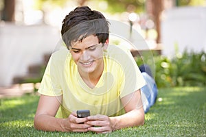 Teenage Boy Laying In Park Using Mobile Phone