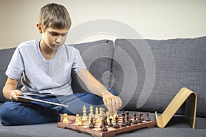 Teenage boy learning to play chess game online with tablet computer at home