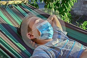 A teenage boy lies on a hammock wearing a protective mask, quarantined during the covid-19 pandemic