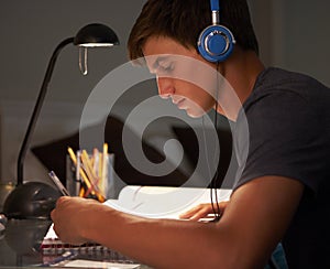 Teenage Boy Listening to Music Whilst Studying At Desk In Bedroom In Evening