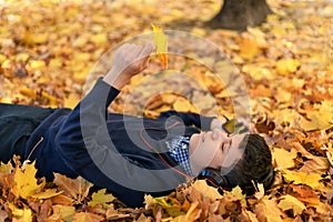 A teenage boy listens to music with headphones, lies on yellow autumn maple leaves, a bright sunny day, beautiful nature in autumn