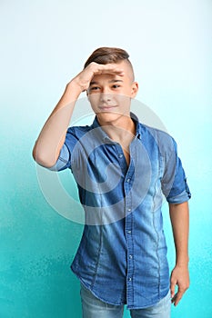 Teenage boy looking faraway on color background
